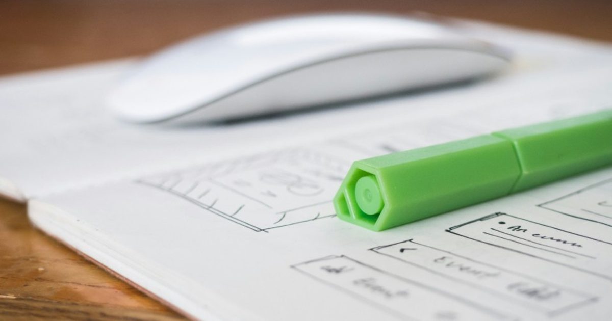 Hand-drawn app wireframes on paper beside a mouse and marker