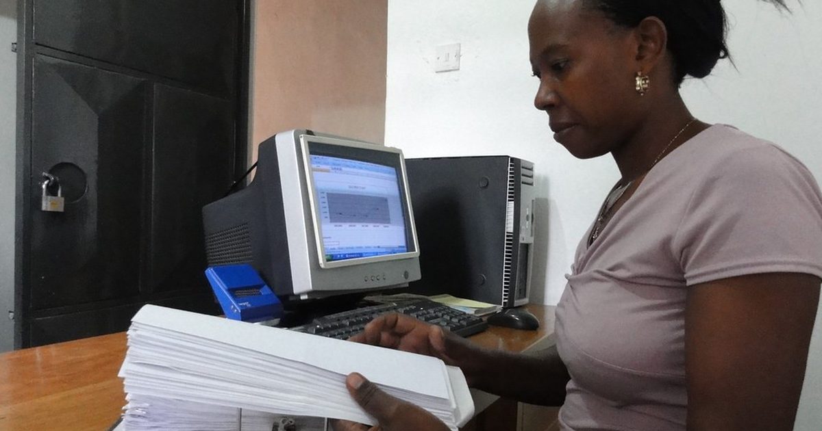 Woman sorting a stack of paper forms beside an office computer